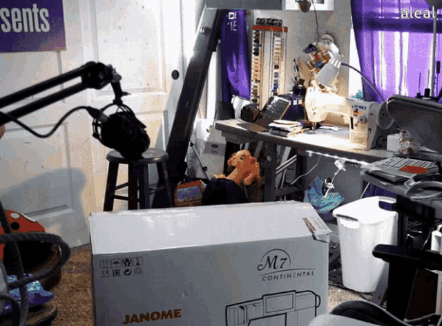 a janome m7 continental sewing machine is sitting in a messy room and a woman pops out of the box